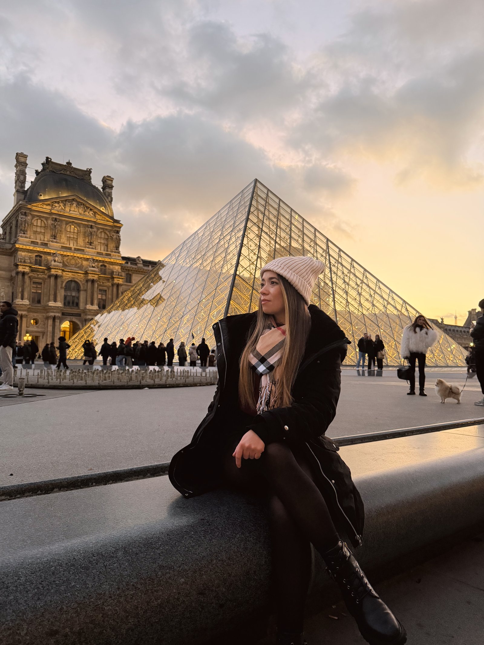 Denise sentada diante da pirâmide do Louvre, em Paris